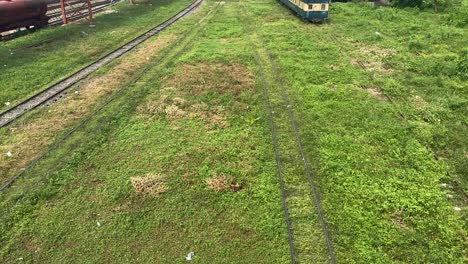 Tilt-up-view-of-an-old-railway-tracks-leading-to-a-loco-shed-on-a-railway-siding-with-thick-undergrowth-and-new-tracks-with-an-over-bridge-in-Komlapur,-Bangladesh