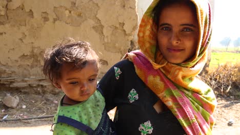 Young-Indian-mother-with-child-in-arms-looking-at-camera-and-smiling,-Noondpura-village-in-Rajasthan