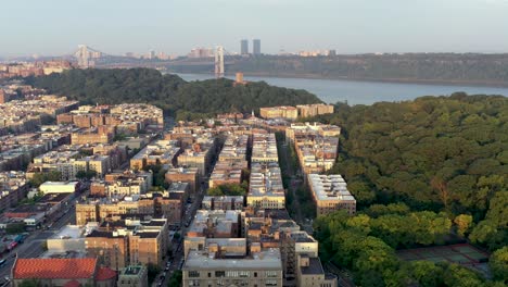 Aerial-rise-over-the-Inwood-neighborhood-of-upper-Manhattan-New-York-City,-the-Cloisters-and-the-George-Washington-Bridge-visible-in-the-distance,-at-golden-hour