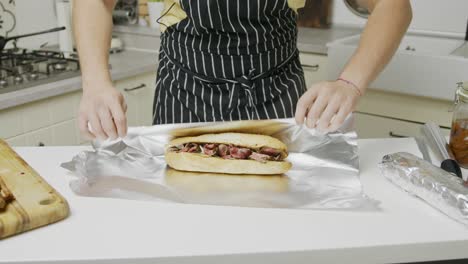 Chef-wraps-freshly-made-beef-sandwich-into-foil-paper-on-kitchen-table