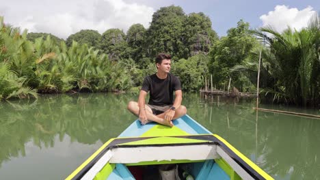 Junger-Kaukasischer-Mann,-Der-An-Einem-Sonnigen-Tag-In-Asien-Auf-Einer-Bootsfahrt-Entlang-Eines-Flusses-In-Ramang-Ramang-Sulawesi-Sitzt,-Umgeben-Von-Mangroven-Und-Grünen-Kalksteinbergen
