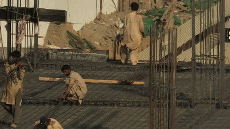 Pakistanische-Männliche-Arbeiter,-Die-Bewehrungsstäbe-Auf-Der-Baustelle-Tragen