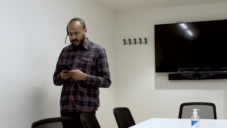 An-Indian-man-pacing-up-and-down-a-boardroom-talking-to-a-colleague-on-his-mobile-phone,-the-man-focused-on-his-conversation-speaking-into-a-microphone-headset-connected-to-his-phone