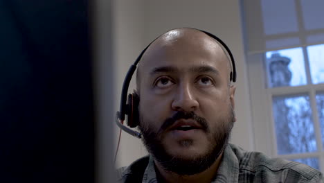 Bald-Ethnic-Minority-Talking-To-Customer-Wearing-Headset-Microphone-Viewed-Behind-Monitor
