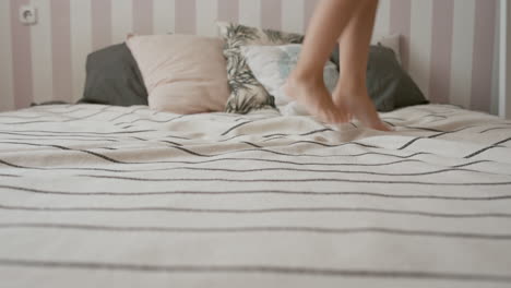 A-young-girl-with-a-doll-in-her-hand-continuously-jumps-on-a-white-stripped-bed