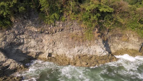 Waves-crashing-onto-cliffs-that-are-covered-with-a-leafy,-tropical-forest-canopy