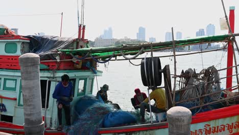 Four-people-fixing-nets-and-then-one-goes-inside-the-cabin,-Pattaya-Fishing-Dock,-Chonburi,-Thailand