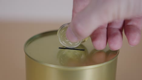 Coins-being-added-to-gold-tin-can-by-hand-in-slow-motion,-Savings-concept