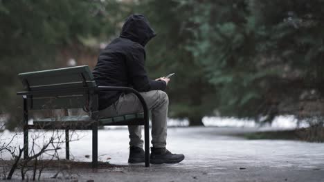 Man-sitting-on-a-bench-and-using-his-phone