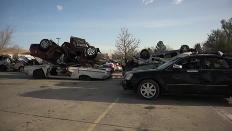 Demolished-and-wrecked-vehicles-stacked-on-top-of-each-other-in-a-parking-lot,-pan