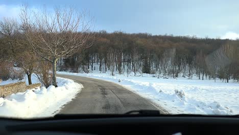 Car-driving-in-stone-old-medieval-village-covered-in-winter-fresh-snow,-mountains-landscape-in-Italian-rural-countryside