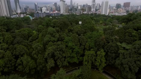 Drone-Volando-Sobre-Un-Bosque-Y-Descubriendo-Kuala-Lumpur-Malasia-Muy-Atrás