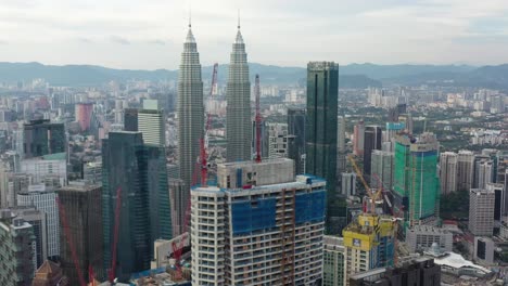 Drone-fly-around-capturing-multiple-building-constructions,-city-development-with-iconic-petronas-twin-towers-in-the-background-with-dense-and-populous-cityscape,-at-downtown-kuala-lumpur,-malaysia