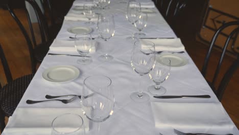 Dining-table-set-for-a-wedding-or-corporate-event-at-fine-dining-restaurant-ceramic-plates-forks-knives-cloth-napkins-on-white-tablecloth-on-table-Steady-Slow-motion-medium-tight