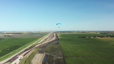 Lone-paragliding-flying-over-rural-agricultural-farm-field-landscape