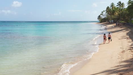 Couple-in-swimwear-stroll-along-tropical-Caribbean-beach