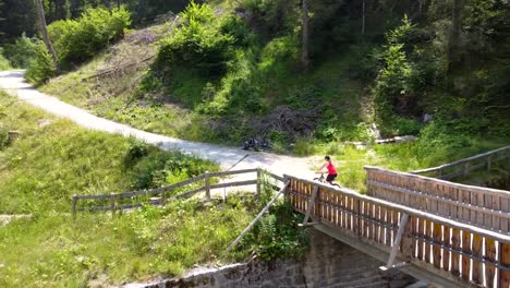 Aerial-shot-chasing-a-women-mountain-biking-past-a-bridge-in-a-mountain-forest