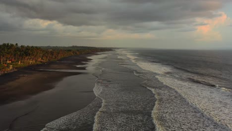 aerial-dolly-zoom-out-of-empty-black-sand-beach-in-Bali-Indonesia-during-sunset