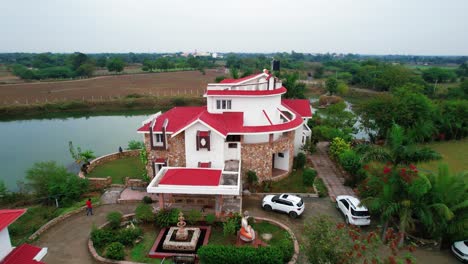 Aerial-drone-shot-traveling-back-of-a-complex-of-beautiful-vacation-homes-in-Vadodara,-India,-surrounded-by-a-calm-lake-and-green-vegetation-for-family-time