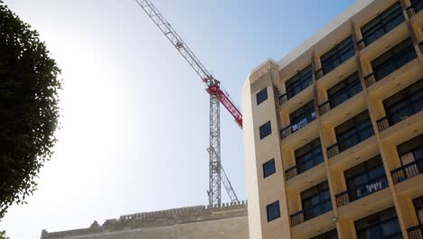 Construction-industrial-tower-crane-working-near-hotel-building-on-windy-day-in-Malta-island,-time-lapse-view