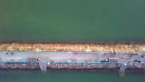A-dynamic-top-down-aerial-shot-of-a-breakwater-jetty-made-out-of-stones-with-a-paved-pathway-for-civilians
