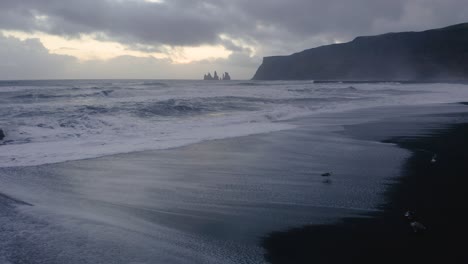 Sunset-at-Reynisdrangar-basalt-columns-and-waves-of-Atlantic-Ocean-hitting-black-sand-beach-at-Vik---birds-finding-food-in-receding-waves