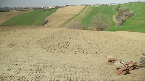 Close-up-of-red-crawler-small-tractor-pulling-triple-rolling-system-preparing-the-land-before-seeding-process-in-Italian-countryside-with-small-scenic-village-on-the-background