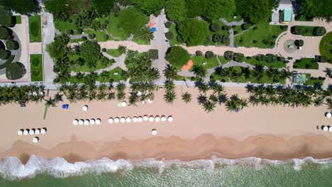 high-altitude-aerial-top-down-view-zooming-onto-the-white-beach-umbrellas-setup-for-tourists-on-the-white-sand-beach-of-Nha-Trang-Vietnam-as-traffic-drives-along-the-coastal-road-on-a-sunny-day