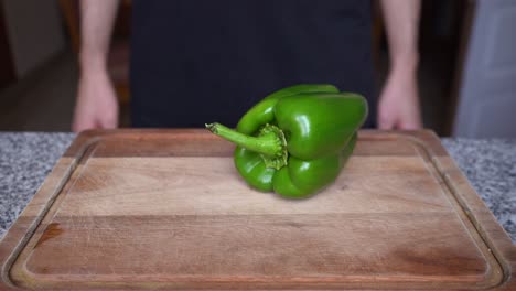 Close-up-of-green-bell-pepper-rolling-on-a-wooden-board