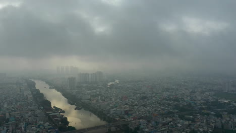 Saigon,-Ho-Chi-Minh-City,-Vietnam-early-morning-drone-footage-flying-a-big-orbit-around-canal-over-districts-four,-seven-and-city-skyline-through-heavy-fog-and-air-pollution-typical-of-southeast-Asia