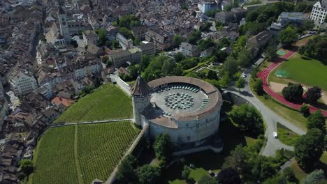 Aerial-orbit-of-Munot-circular-fortification-in-verdant-hill-next-to-High-Rhine-river-and-Schaffhausen-village-between-woods,-Switzerland