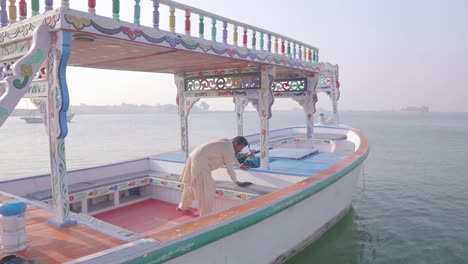 Worker-Wiping-Down-Seats-On-Sightseeing-Boat-At-Keenjhar-Lake-In-Thatta,-Pakistan