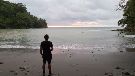 a-man-looking-at-the-ocean-at-sunset-on-the-beach-of-playa-la-vaca-in-costa-rica-on-a-cloudy-day
