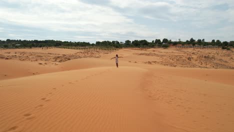 slow-low-aerial-of-footsteps-in-the-sand-as-woman-walks-top-of-dunes-in-desert