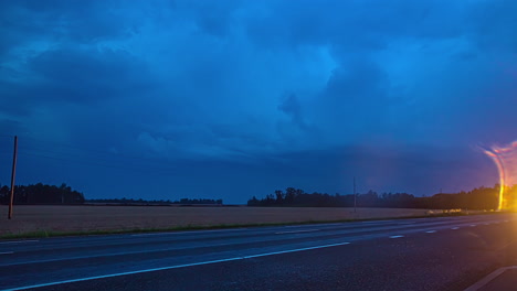Timelapse-shot-of-cars-driving-of-highway-along-rural-landscape-with-lightning-visible-in-the-background-along-dark-cloud-moving-in-evening-sky