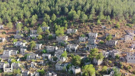 wide-aerial-shot-panning-around-abandoned-buildings-in-ruin-at-the-famous-greek-village-of-kayakoy-located-in-the-forest-of-a-mountain-in-Fethiye-Turkey-on-a-summer-day