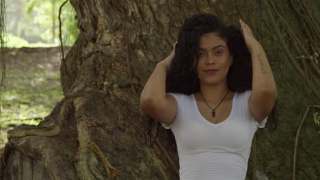 Close-up-of-sexy-young-hispanic-model-playing-in-her-hair-standing-in-front-of-a-large-tree