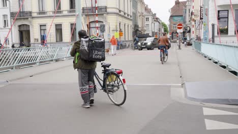 Uber-Eats-delivery-rider-with-mechanical-problem-walking-next-to-bike-in-the-crowded-city---Ghent,-Belgium