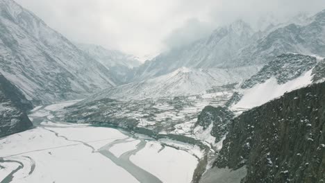 Filmische-Luftaufnahme-Des-Schneebedeckten-Dorfes-Hussaini-Im-Hunza-tal-Neben-Dem-Zugefrorenen-Fluss