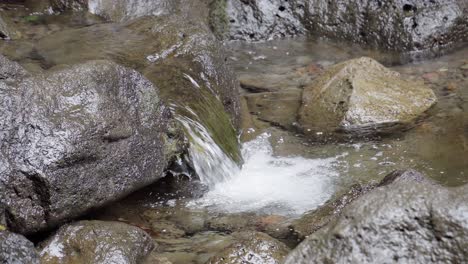Ein-Kleiner-Bach-Mit-Schwarzen-Felsen-In-Der-Nähe-Eines-Wasserfalls