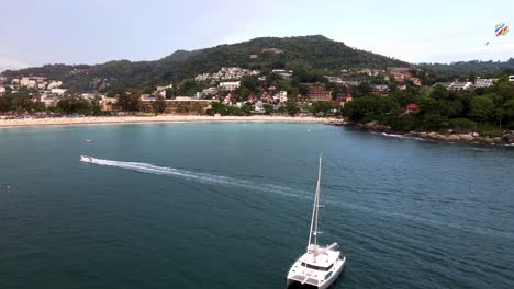 Aerial-Flying-Over-White-Yacht-With-Parasailer-Going-Past-At-Over-Kata-Beach-In-Phuket