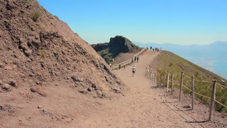 Panning-across-path-and-people-hiking-along-the-crater-of-the-Mount-Vesuvius-volcano-near-Pompeii,-Italy