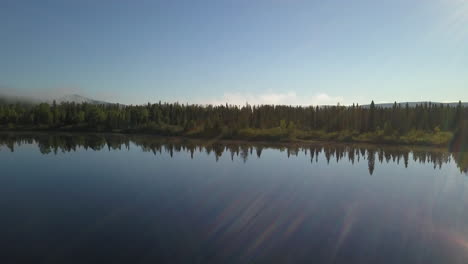 Aerial-shot-panning-left-over-a-calm-watered-lake-facing-a-beautiful-forest-in-northern-Ontario-Canada