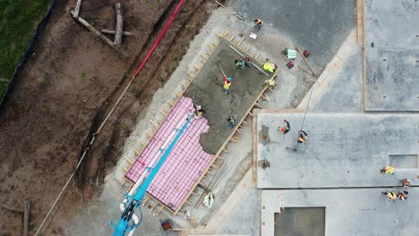 Overhead-View-Of-Workers-And-Cement-Pump-Truck-Long-Arm-Pumping-Cement-Mix-On-Floor-Surface-Of-Building-Under-Construction