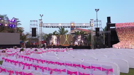 Seating-decoration-on-wedding-stage-aerial-drone-fly-over-garden-pink-venue,-sound-system-and-led-screen