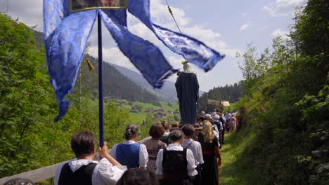 Female-worshippers-in-traditional-Tyrolean-costumes-carry-the-Virgin-mary-and-a-blue-banner-in-a-mountain-landscape-during-a-religious-procession