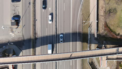 Top-Down-Aerial-View-of-Highway-Traffic-and-Pedestrian-Bridge-Overpass-on-Sunny-Autumn-Day,-High-Angle-Drone-Shot