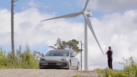 Ein-Tesla-Model-3-Und-Sein-Besitzer-Vor-Einer-Windkraftanlage