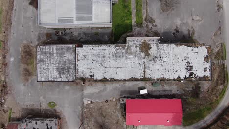 Top-Down-Aerial-Drone-Footage-Moving-Left-over-a-Large-Abandoned-Building-with-a-Decaying,-Overgrown-Roof