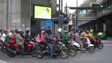 Mucha-Gente-Montando-Motocicletas-En-El-Semáforo-En-Rojo-En-Un-Cruce-Concurrido-En-Bangkok